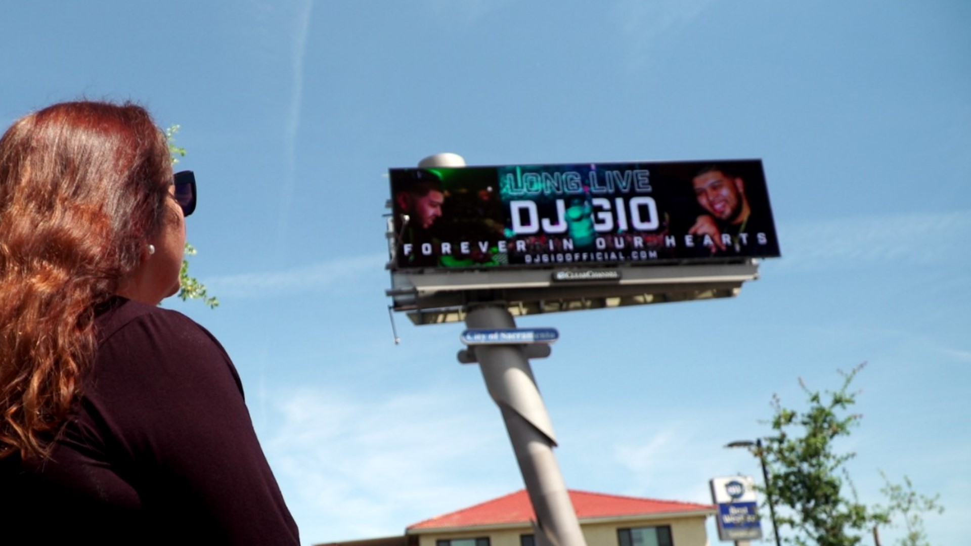 The billboard shows DJ Gio smiling and performing in front of a large crowd with the words "Long Live DJ Gio" and "Forever in our hearts."